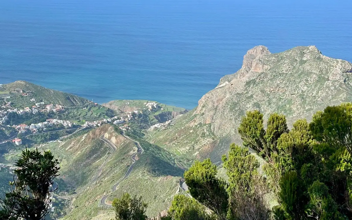 Green Anaga ridges with a white village on the slopes, a winding road and a rocky peak above the blue ocean