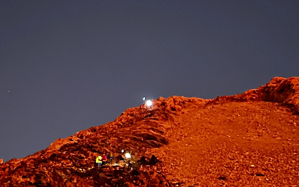 Headlamps of a hiking group on a rust-red volcanic ridge at night