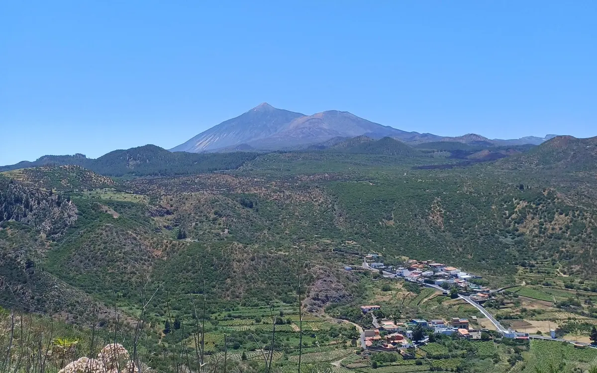 Il cono del Teide all'orizzonte sopra una valle verde con un villaggio e campi terrazzati