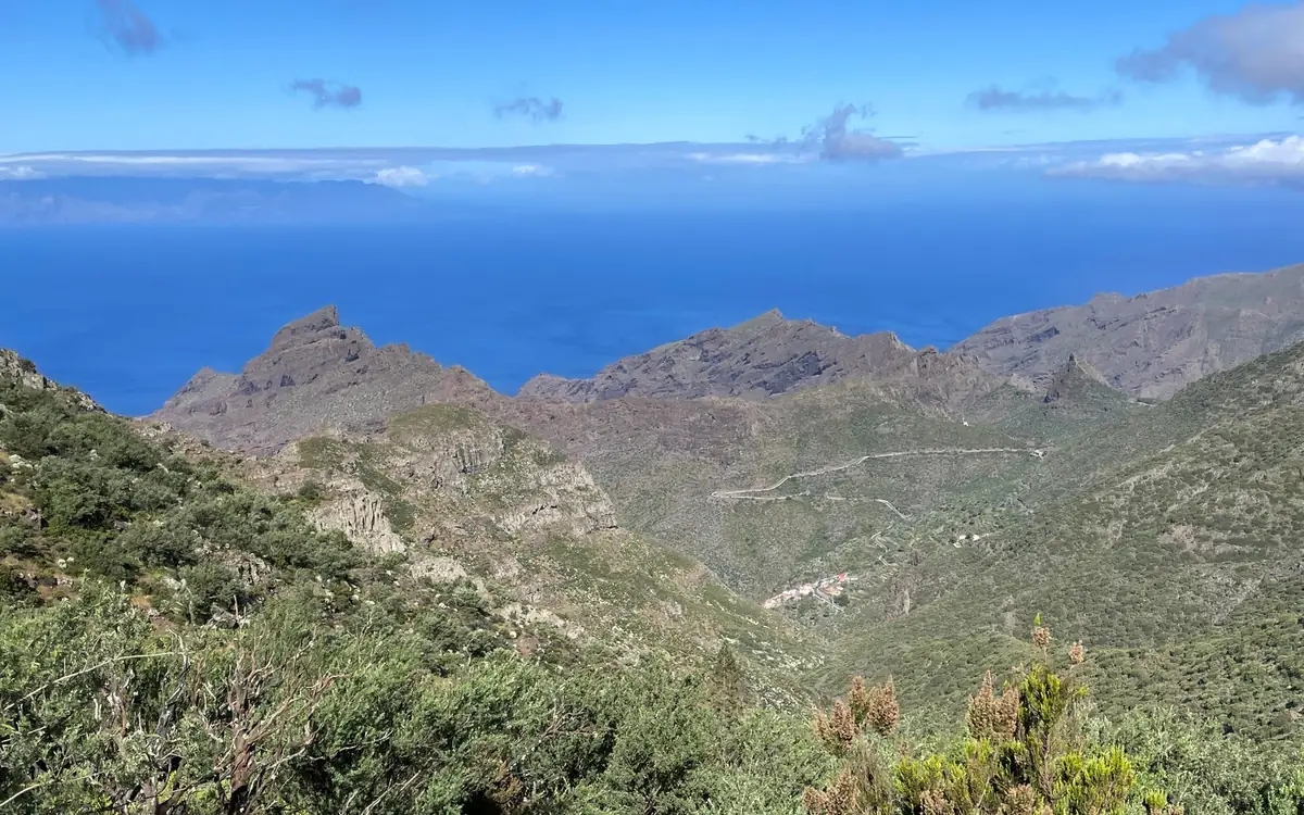 Cresti frastagliati sopra l'oceano, macchia verde davanti e una strada che serpeggia sul pendio